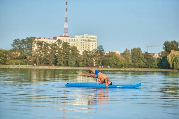 Jongen doen yoga oefeningen tijdens het zwemmen op paddle board in lake. — Stockfoto