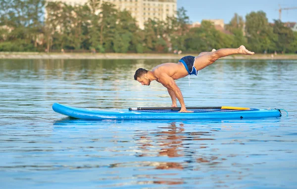 Hombre practicando yoga, haciendo balanceo de peso corporal sobre tabla de paddle . — Foto de Stock