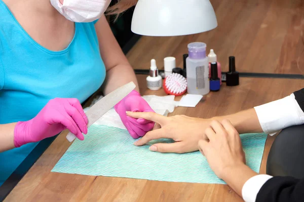 Professional manicurist in gloves and mask polishing nails of female customer. — Stock Photo, Image