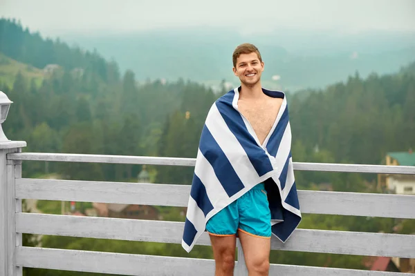 Guy standing on wooden terrace of mountain resort.