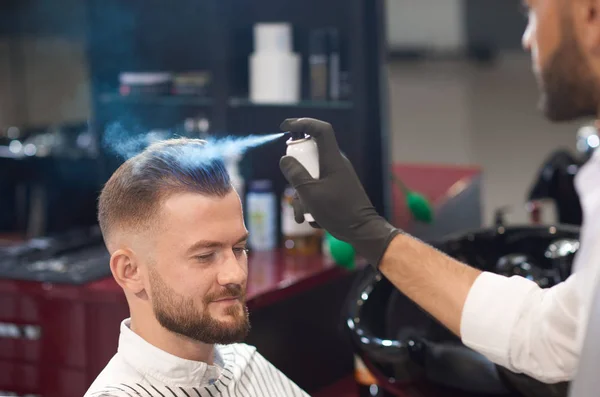Парикмахер фиксирует волосы мужчины с помощью спрея в парикмахерской — стоковое фото