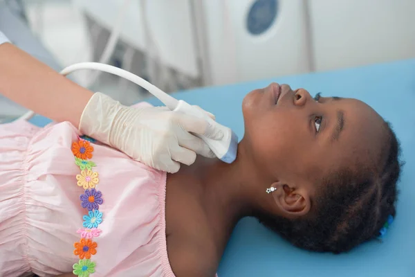 Pequena menina afro deitada na cama enquanto ultra-som da tireóide . — Fotografia de Stock