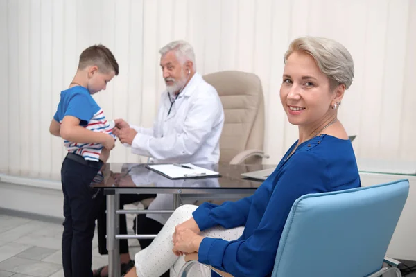 Madre sonriendo, esperando al doctor examinando a su hijo . —  Fotos de Stock