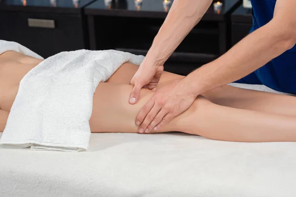 Manos de masajista masajeando cuádriceps de hembra en salón de spa — Foto de Stock