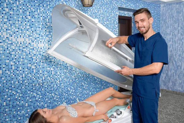 Médico em pé perto da cama de bronzeamento e posando no salão de spa — Fotografia de Stock