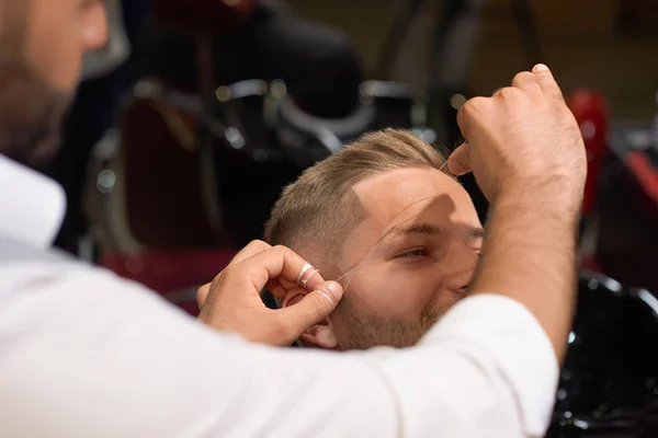 Парикмахер делает процедуру резьбы бровей в парикмахерской — стоковое фото