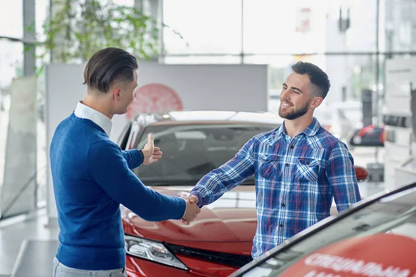 Two men standing in salon between cars and shaking hands.