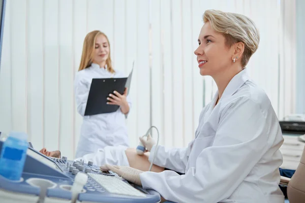 医生办公室里从事病人工作的妇女的侧视图 为预防疾病提供体检的出血不漏的精神主义者 年轻的站着写一些细节 — 图库照片