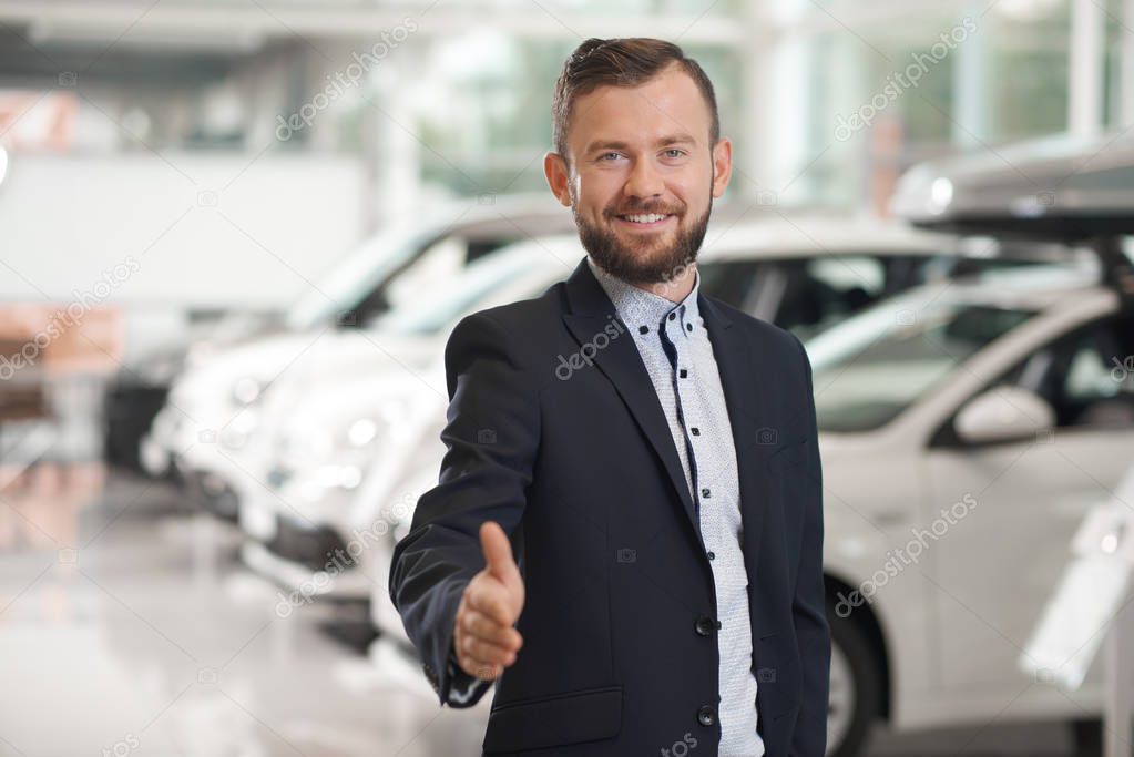 Car dealer in suit posing in car center.