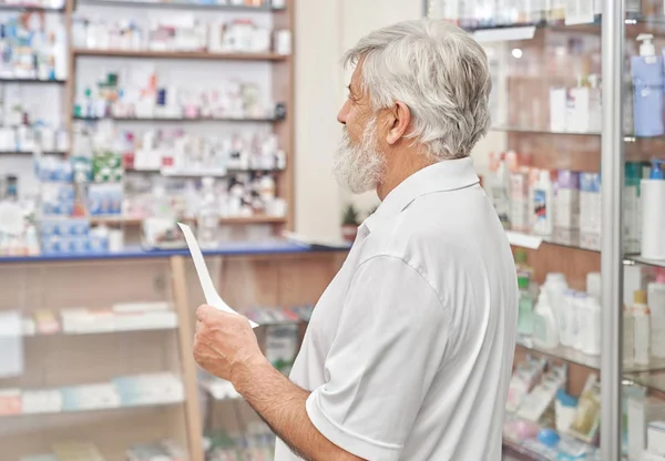 头发花白 留胡子的老人站在药店里 手里拿着药方 老人在化学家商店里寻找药物和补救措施 养老金领取者看药店货架 — 图库照片