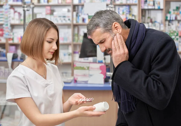 Farmacéutico ayudando a hombre con dolor de muelas en farmacia . — Foto de Stock