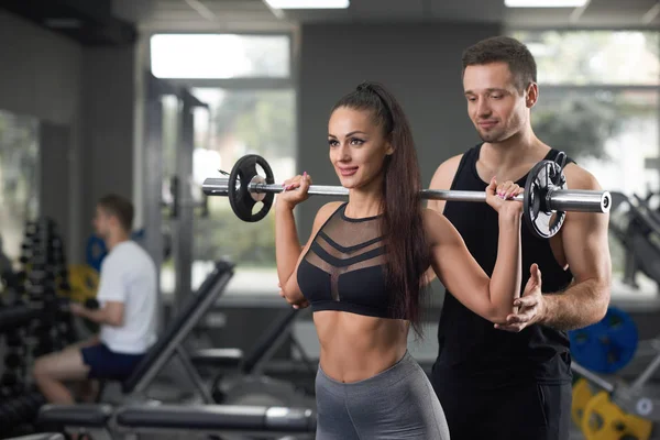 Mulher bonita levantando barbell e treinador posando no ginásio . — Fotografia de Stock