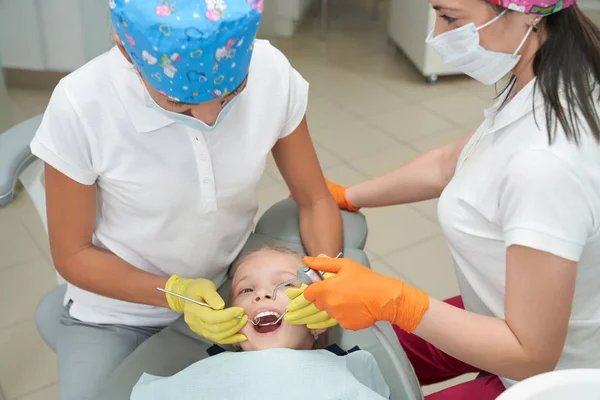 Chica tumbada en la silla con la boca abierta y mirando a los dentistas — Foto de Stock