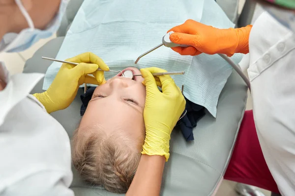Menina ling na cadeira dental, enquanto dois dentistas tratando dentes — Fotografia de Stock
