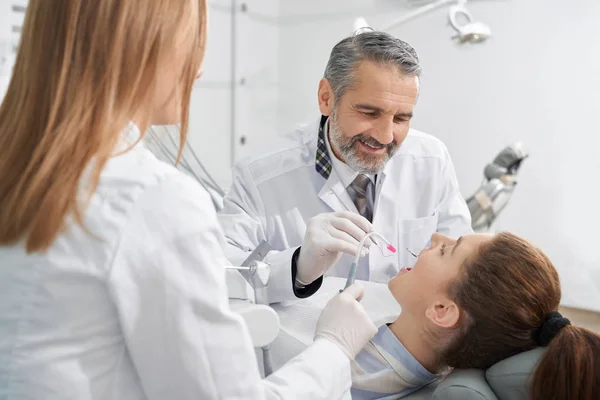 Vista do lado do dentista masculino positivo que trata os dentes — Fotografia de Stock