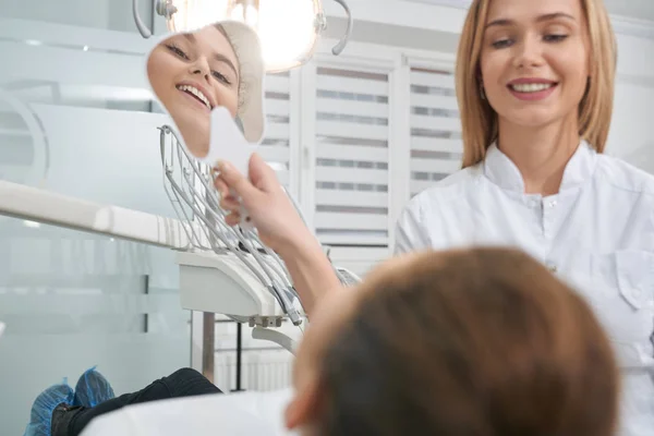 Mujer en silla de dentista mirando al espejo, sonriendo . — Foto de Stock