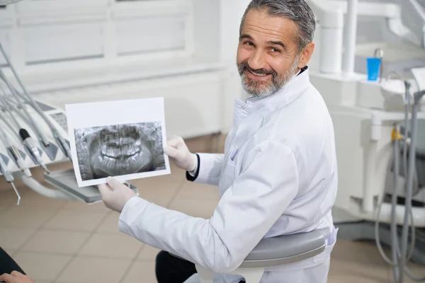 Dentista che mostra i raggi X della mascella, sorridente e in posa . — Foto Stock