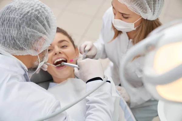 Dentists using retoration tools to woman with opened mouth.