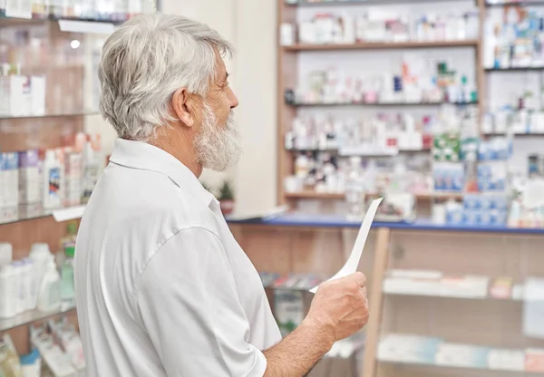Hombre mayor eligiendo medicamentos en farmacia . — Foto de Stock