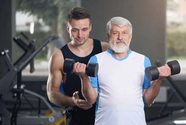 Uomo anziano e allenatore in posa con i manubri in palestra . — Foto Stock