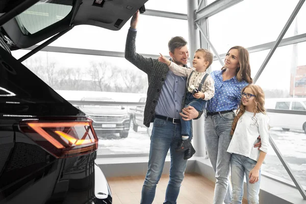 Família feliz olhando para o tronco de carro preto caro . — Fotografia de Stock