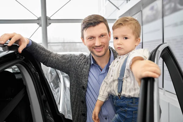 Far poserar med son nära auto i bilfirma. — Stockfoto