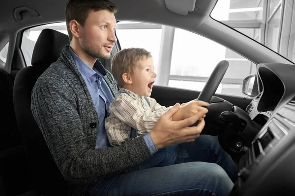 Pieni poika istuu isän kanssa kuljettajan istuimella uudessa autossa. . — kuvapankkivalokuva