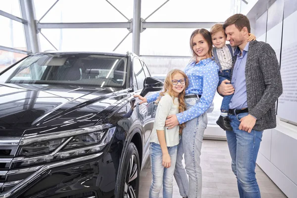 Rodina představuje poblíž černé auto v autorizovaném autosalonu. — Stock fotografie