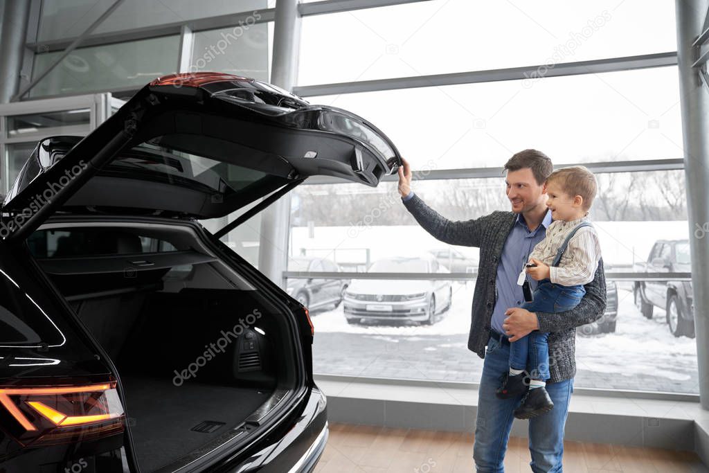Father opening car trunk, showing auto to son.