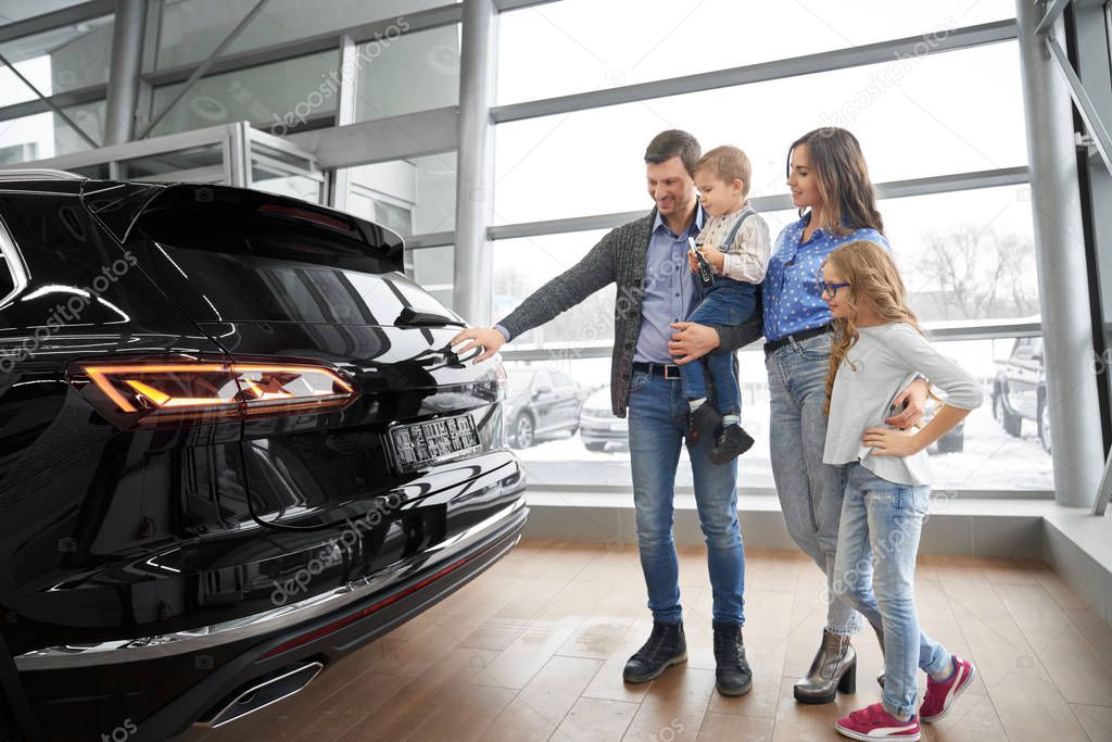 Family observing new black car in showroom.