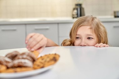 Child secretly taking american cookies from plate. clipart