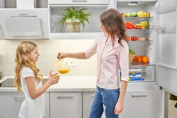 Mãe derramando suco de laranja, filha segurando vidro . — Fotografia de Stock