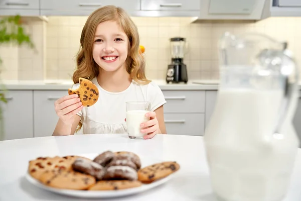 Девушка сидит за столом, держа стакан молока и печенье . — стоковое фото
