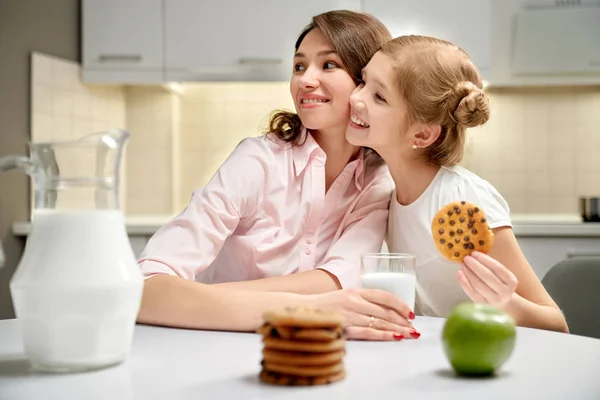 Mãe e menina sentados na mesa da cozinha com biscoitos e mik . — Fotografia de Stock