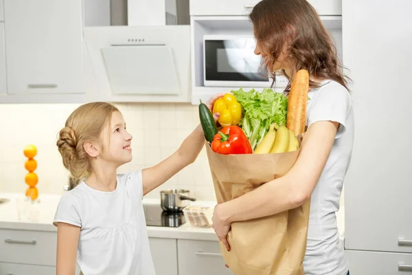 Мама держит бумажный пакет с продуктами, стоя с дочерью — стоковое фото