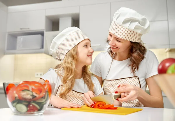 Filha e mãe em chapéus chef cozinhar salada de legumes . — Fotografia de Stock