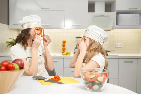 Funny mom and daughter holding pepper slices as glasses.