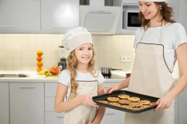 Мама и дочь в фартуках и шляпах шеф-повара позируют с печеньем — стоковое фото