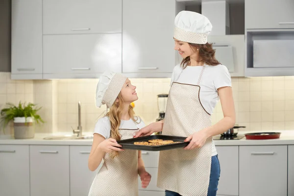 Lovely mom and child holding baking sheet with cookies.