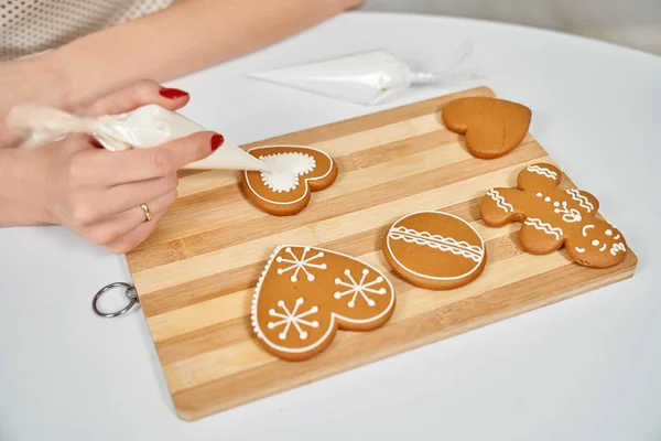 Mãos femininas decorando biscoitos de gengibre com esmalte de açúcar . — Fotografia de Stock