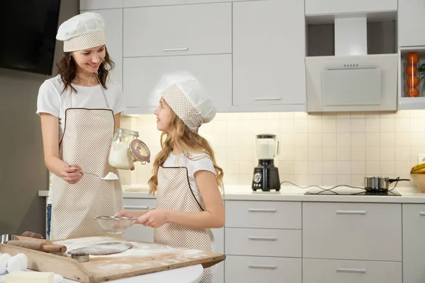 Fille et mère dans des tabliers tamisant la farine pour les biscuits . — Photo