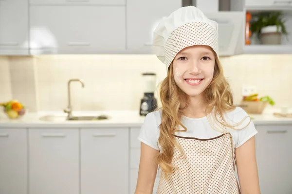 Menina feliz no avental e chapéu chef posando na cozinha . — Fotografia de Stock