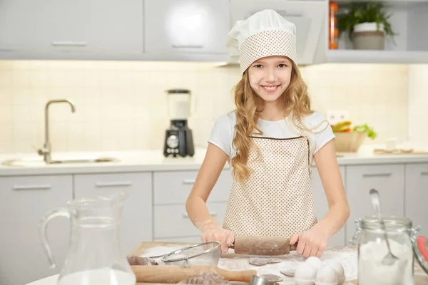 Pretty girl in chef hat cooking biscuits on kitchen. Stock Photo