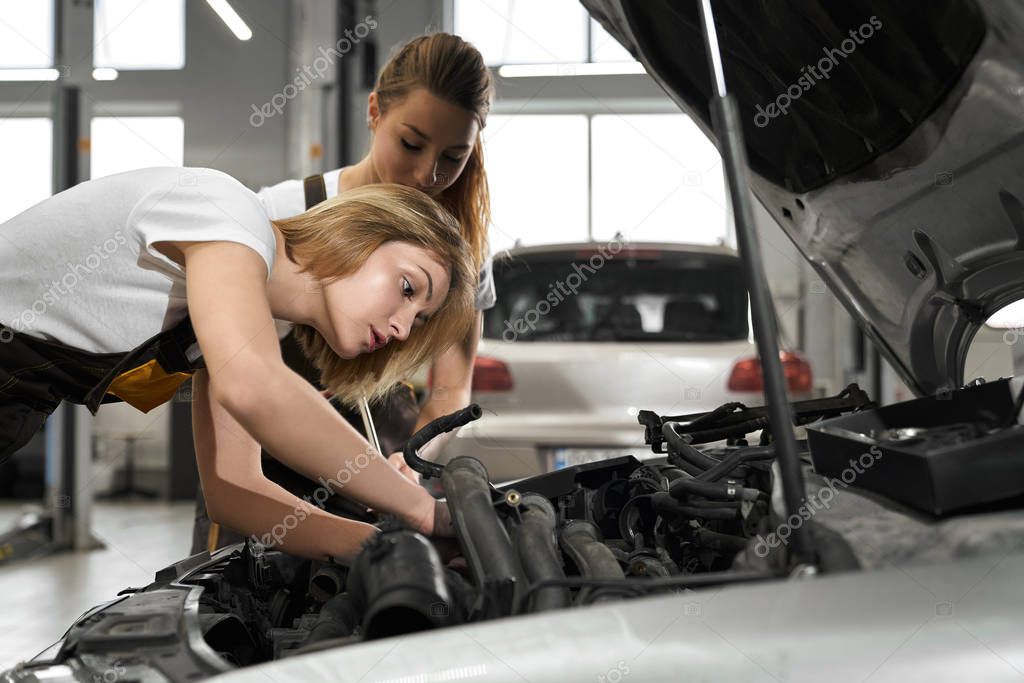Two girls mechanics and fixing automobile.