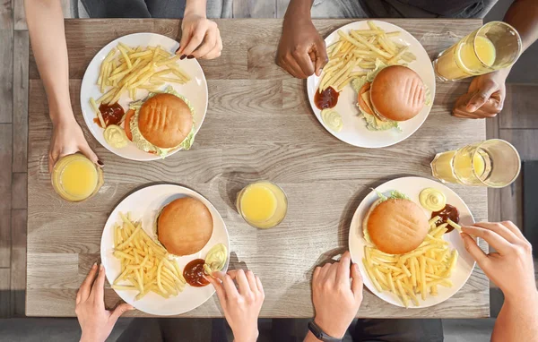 Plates of hamburgers, french fries, juice glasses on table.