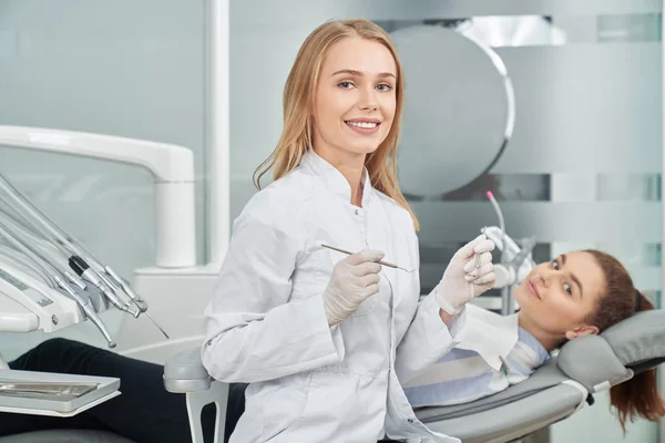 Dentista femenina con abrigo blanco posando, sonriendo cerca del cliente . — Foto de Stock