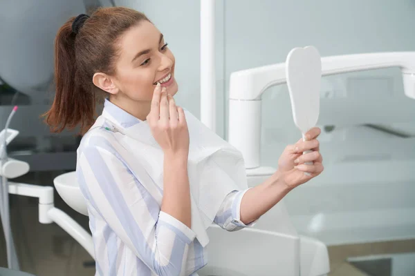 Mulher feliz olhando para o espelho na clínica odontológica . — Fotografia de Stock
