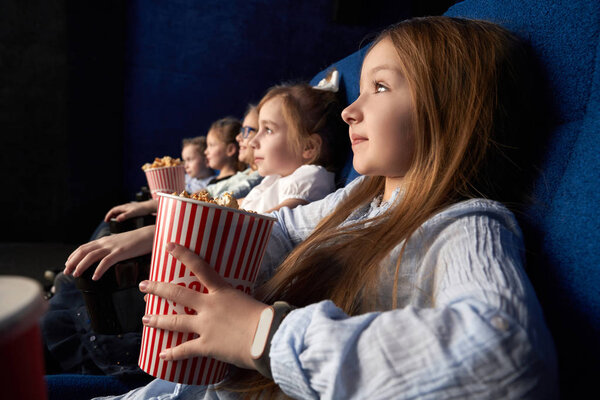 Little girl with friends sitting in cinema.