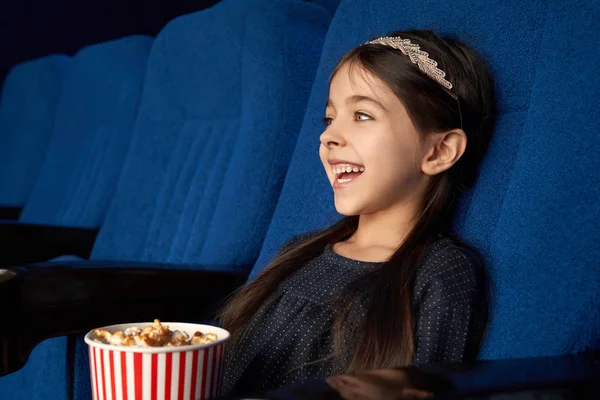 Gioiosa bambina che guarda film, ridendo al cinema . — Foto Stock