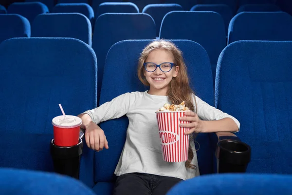Радостная девушка держит ведро попкорна, позирует в кино . — стоковое фото